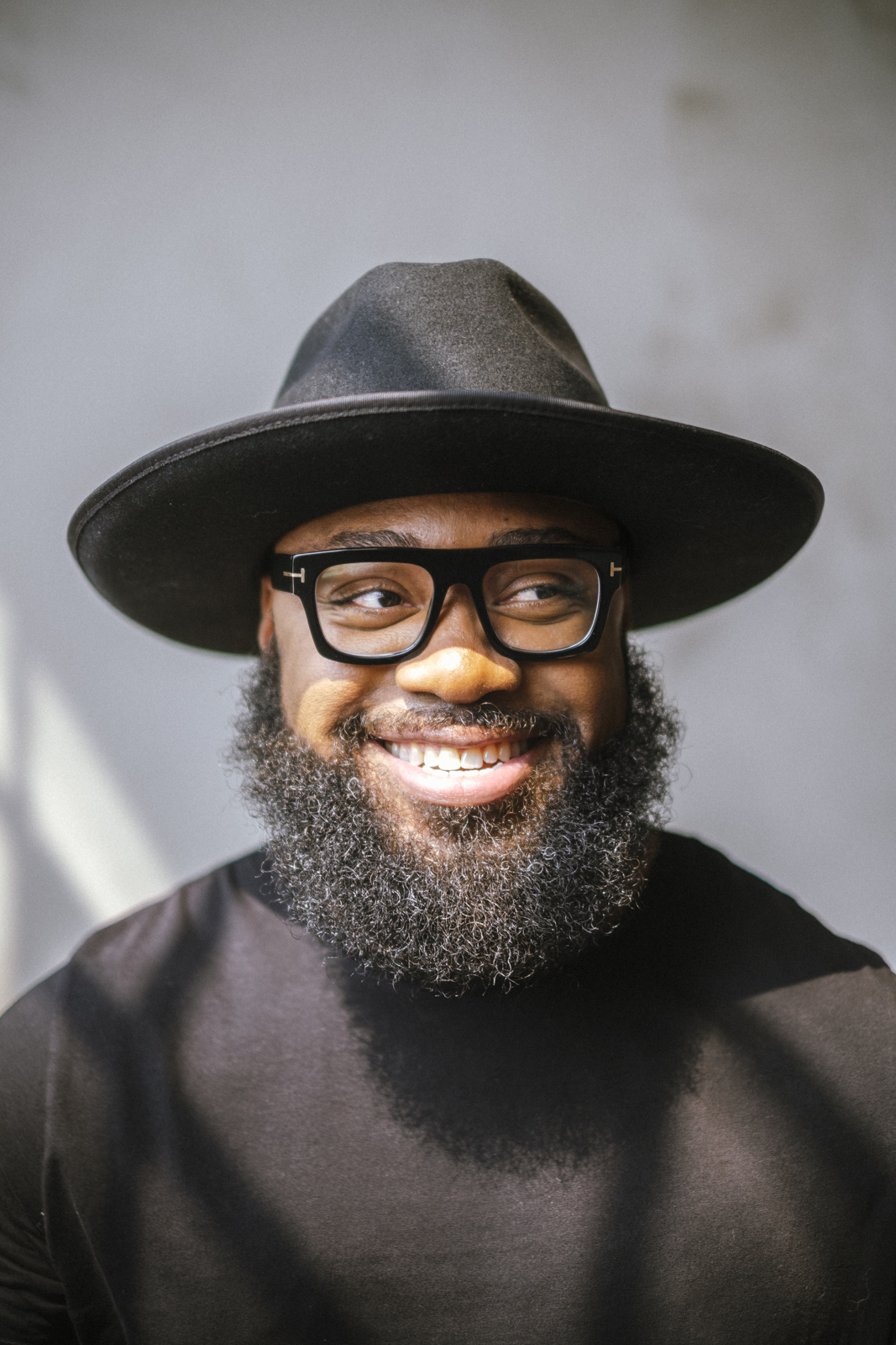 Portrait of a man in a black hat and glasses smiling against a neutral backdrop