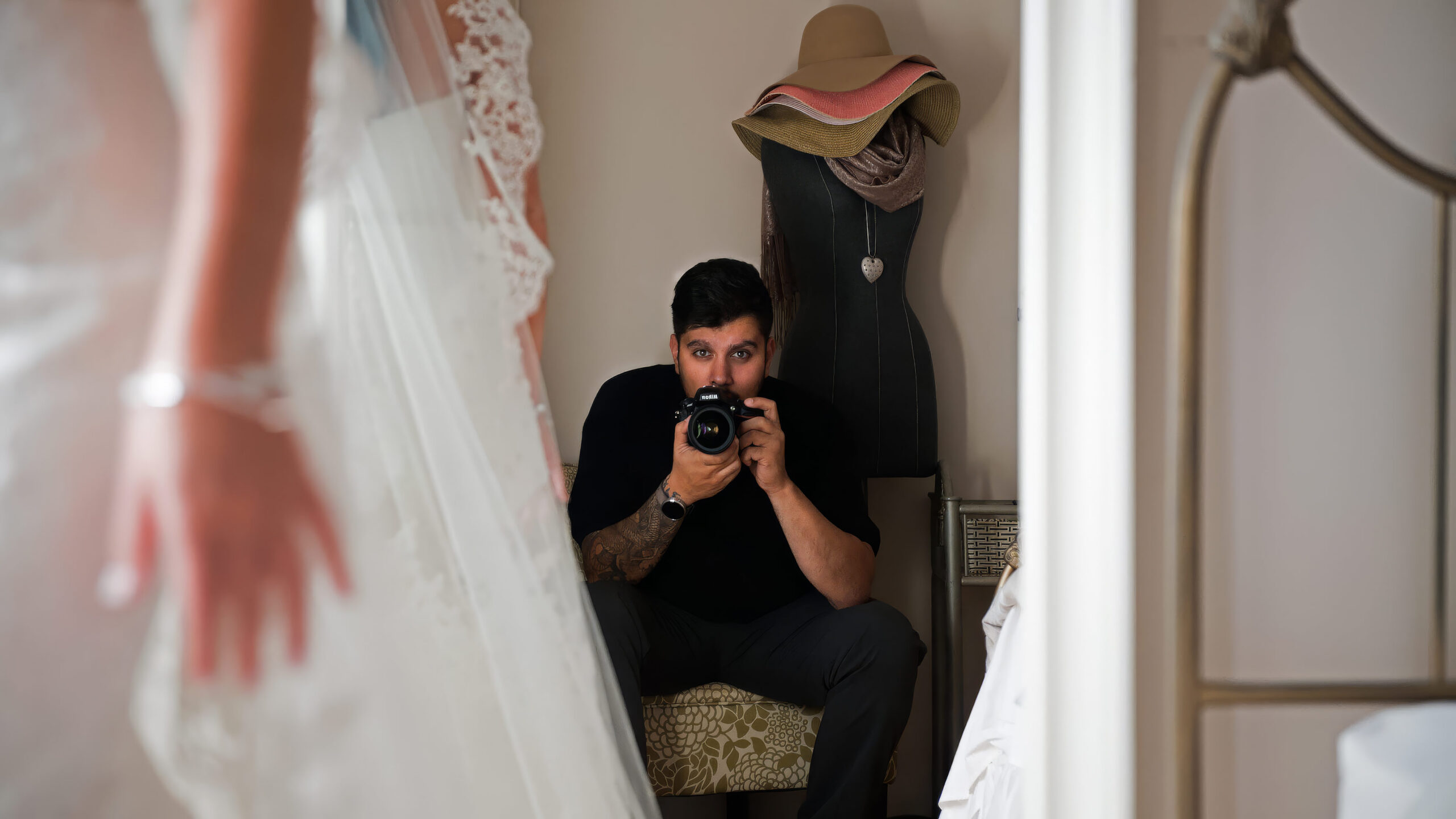 Reza photographing a bride getting ready, camera in hand, reflected in a mirror